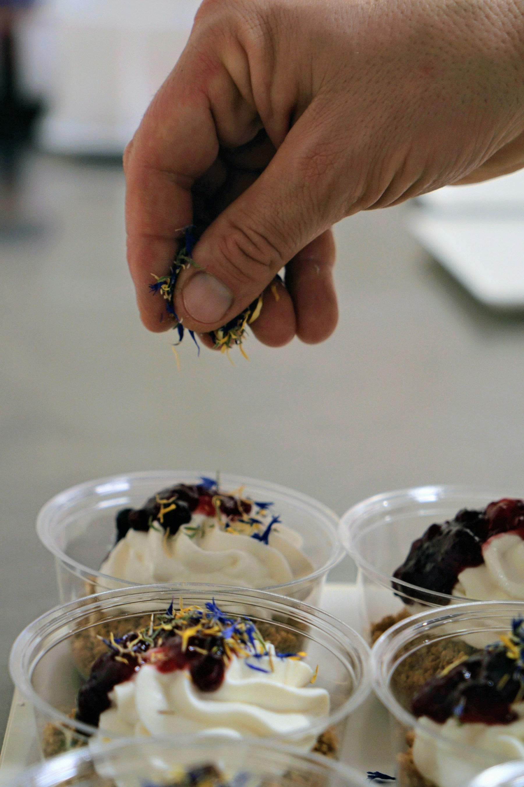 A hand finishing individual desserts with flower petals